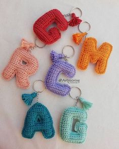 crocheted keychains with letters and tassels are arranged on a white surface