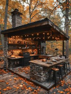 an outdoor kitchen in the woods surrounded by trees and leaves with lights strung over it