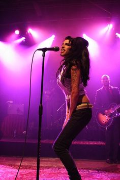 a woman standing in front of a microphone on top of a stage with purple lights