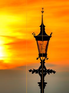 a street light with the sun setting in the back ground behind it, and an orange sky