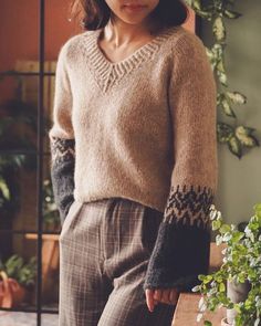 a woman standing next to a plant wearing a sweater