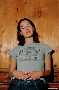 a woman sitting on the floor in front of a wooden wall with her hands crossed