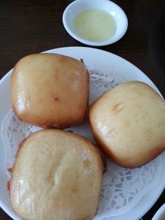 three doughnuts on a white plate next to a bowl of dipping sauce