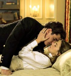 a man and woman laying on top of a bed next to each other in front of a chandelier