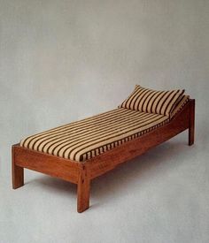 a wooden bed with striped sheets and pillows on it's headboard, against a white wall