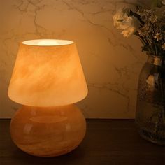 a table lamp sitting on top of a wooden table next to a vase filled with flowers