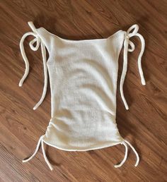 the back of a white top with ties on it sitting on a wooden floor next to a pair of scissors