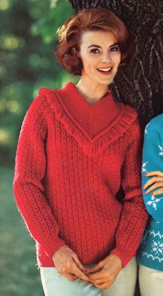 two women standing next to each other in front of a tree wearing red sweaters