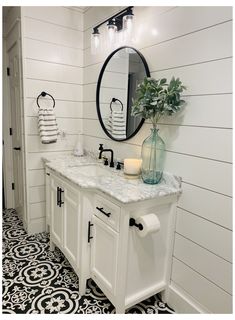 a white bathroom with black and white flooring, two sinks and a large round mirror on the wall