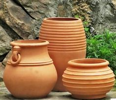 three clay pots sitting next to each other in front of a stone wall and grass