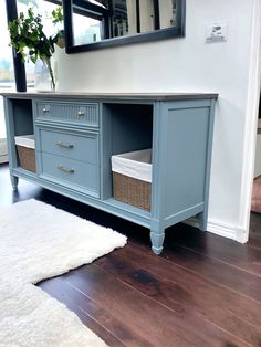 a blue dresser with drawers and baskets on top in a room next to a mirror