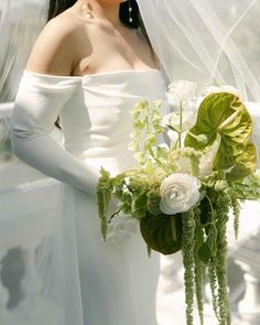 a woman in a white dress holding a bouquet of flowers and greenery on her wedding day