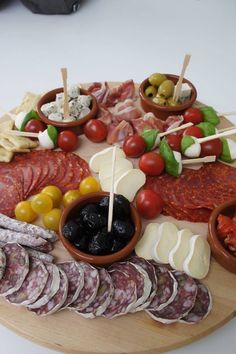 an assortment of meats and cheeses on a wooden platter with olives