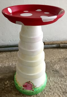 a red and white mushroom shaped plate on top of a stack of plastic plates in front of a wall