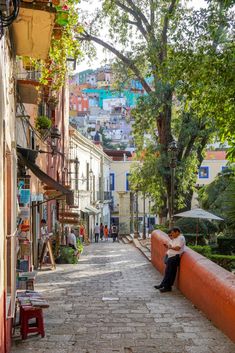 a man sitting on a bench in the middle of an alleyway with buildings behind him