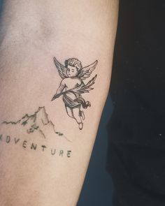 a small tattoo on the arm of a man with an angel above it that says adventure