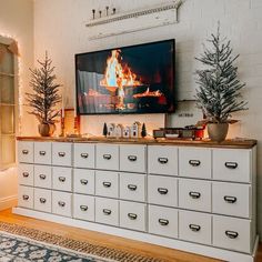 a flat screen tv mounted on top of a white dresser next to a christmas tree