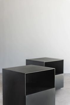 two black tables sitting next to each other on top of a cement floor in front of a white wall