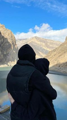 a person sitting on the edge of a cliff looking out over a body of water with mountains in the background