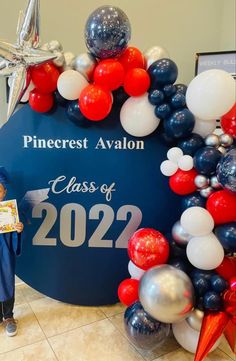 a boy standing in front of a graduation balloon arch