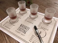 four shot glasses sitting on top of a wooden table next to a pen and paper