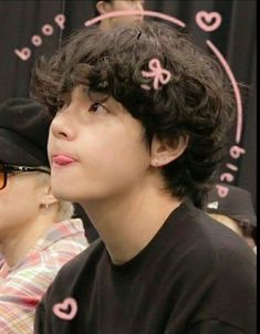 a young man with curly hair wearing a black shirt and pink bow on his head