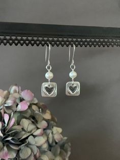 "White Pearl Earrings, Square Sterling Silver and Fresh Water Pearl Dangle Earrings, Heart Earrings, Bridesmaid Gift, Bride, Wedding Gift Simple but, elegant earrings. They are adorned with sterling silver heart charms and fresh water pearls.  Lightweight and versatile. Perfect for everyday and would be beautiful on a bride, gift for bridesmaid or mother of bride.  Pearls are known as the \"stone of sincerity\", it signifies faith, and purity. They are said to help with fertility and work as a calming stone by getting rid of negative energy. Fresh Water Pearls are also known for promoting sincerity truth, and loyalty.  We use only fine and sterling silver for all of our jewelry and findings, including our handmade earwires. Our unique hand forged metalwork is shaped and hammered for simpli Silver Heart Earrings With Pearl Drop For Gift, Valentine's Day Silver Pearl Drop Earrings, Heart-shaped Pearl Earrings For Anniversary On Valentine's Day, Bride Pearls, White Heart-shaped Earrings With Pearl Charm, Matte Black Jewelry, Silver Heart-shaped Pearl Earrings For Valentine's Day, Bride Wedding Gift, Gold Diamond Hoop Earrings