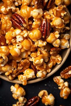 a wooden bowl filled with caramel popcorn kernels on top of a black surface