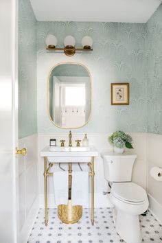 a white toilet sitting next to a sink in a bathroom under a mirror and gold faucet