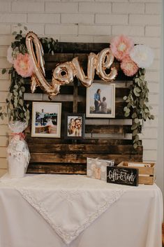 a table topped with pictures and balloons in front of a love sign on top of a wooden pallet