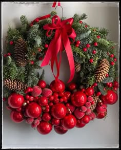 a christmas wreath hanging on the wall with red berries and pineconis around it