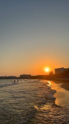 the sun is setting at the beach with people in the water