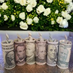 five rolled up money sitting on top of a table next to flowers and a vase