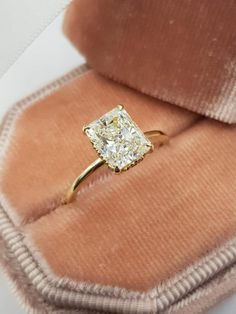 an engagement ring with a cushion cut diamond sits in a velvet case on top of a pink velvet pillow