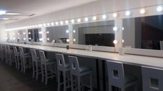 a long white counter topped with lots of stools and lights in a room filled with mirrors