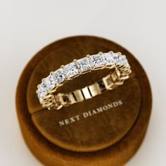 a diamond ring sitting on top of a wooden display stand in a jewelry box with the words next diamonds written below it