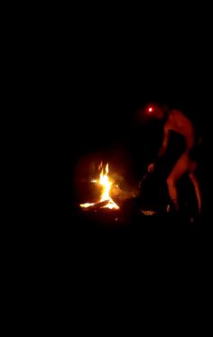 a man standing next to a fire in the dark