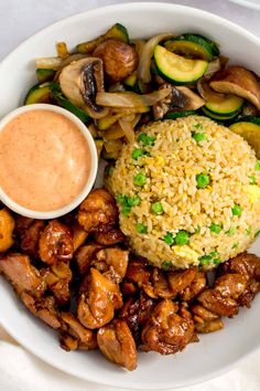 a white plate topped with meat and rice covered in sauce next to veggies