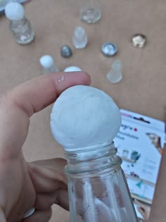 a hand holding a small glass jar with white stuff in it next to other items