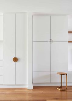 an empty room with white cupboards and wooden flooring on the side, along with a stool