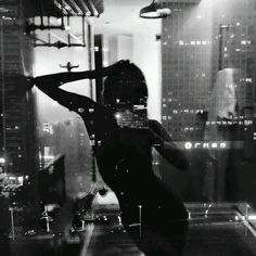 a woman standing in front of a window next to tall buildings