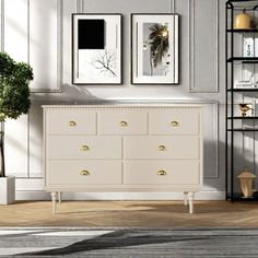 a white dresser sitting in a living room next to a book shelf and potted plant