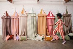 a woman standing in front of several colorful curtains and pillows on the floor with her arms out