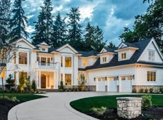 a large white house with lots of windows and trees in the front yard at dusk