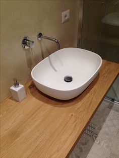 a white bowl sink sitting on top of a wooden counter next to a glass shower door