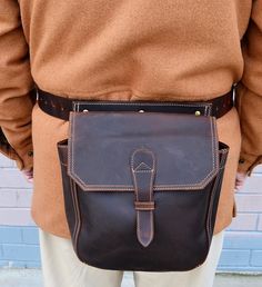 a man wearing a brown jacket and tan pants is holding a black leather messenger bag