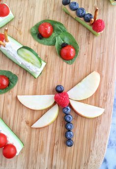 a wooden cutting board topped with fruit and veggies shaped like a dragon's wings