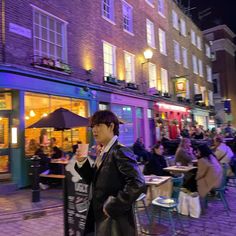 a man standing on the sidewalk in front of a building with people sitting at tables