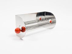 a metal object with two cherries attached to it's sides on a white surface