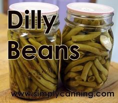 two jars filled with green beans sitting on top of a wooden table